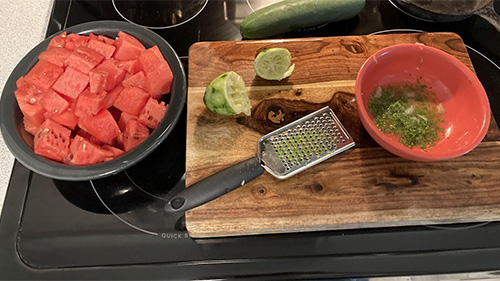 watermelon, lime, grater, and a bowl on a cutting board