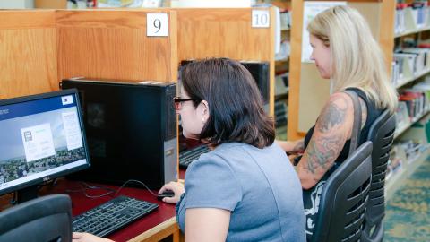 Two women at desktops in a library.