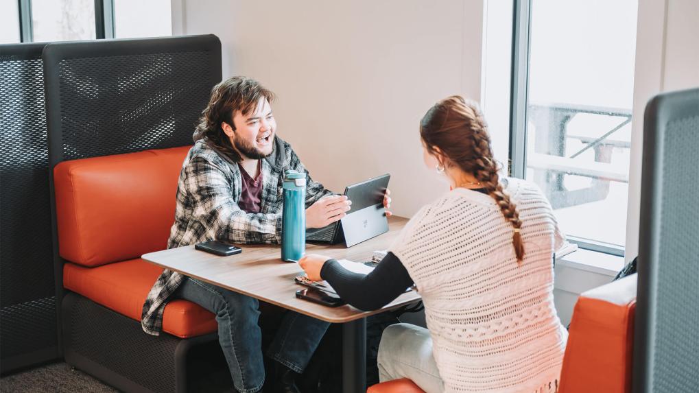 Two people sitting in a booth and talking at a library.