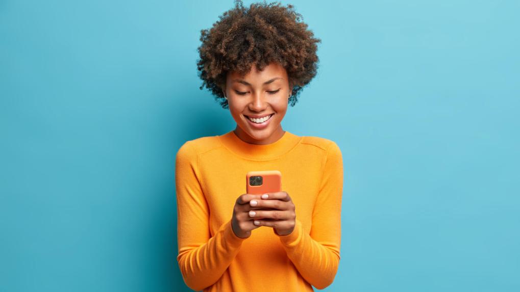 Subscribe to our newsletters Woman smiling while texting on her phone.