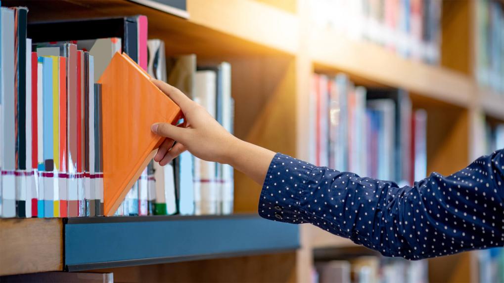 Hand taking a book of a library shelf. 