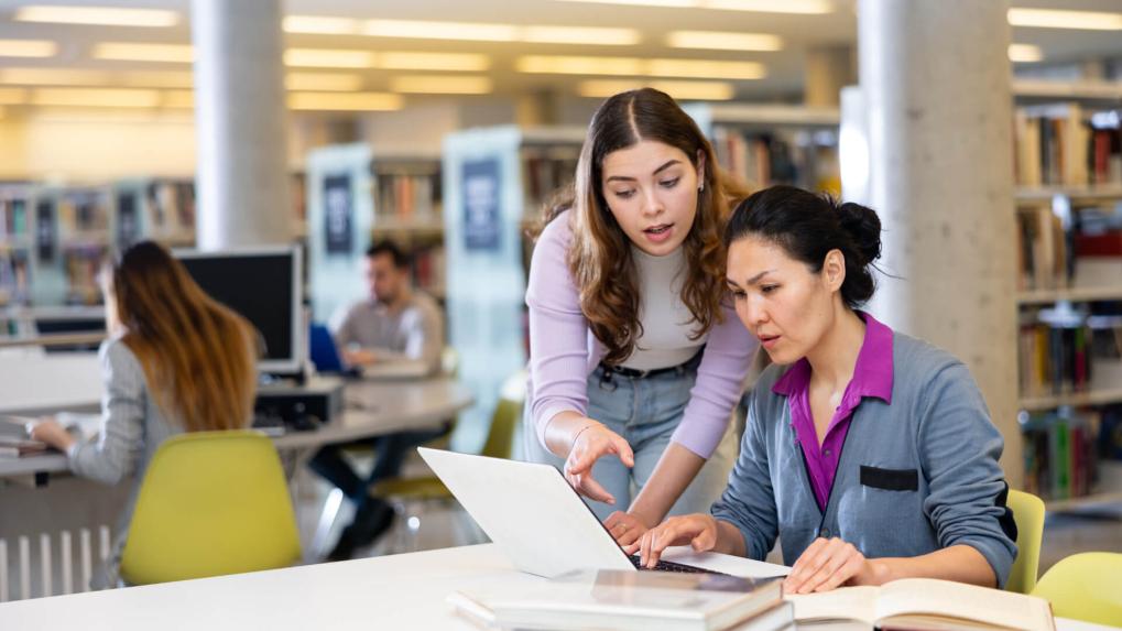 Woman helping a woman on her laptop in a library
